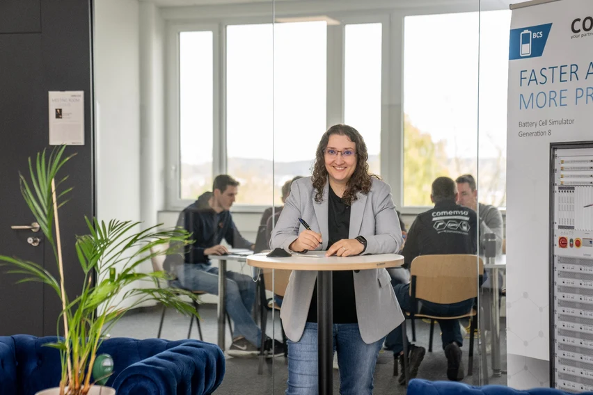 Colleague taking notes with a team meeting visible behind her at comemso.
