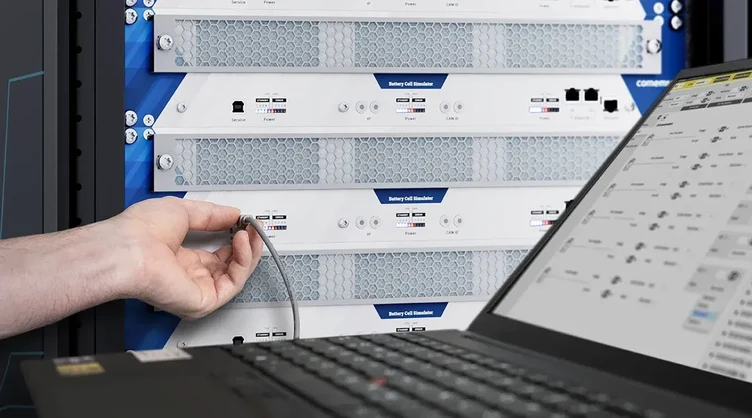 Close-up of an engineer connecting a rack-based Battery Cell Simulator beside a laptop.