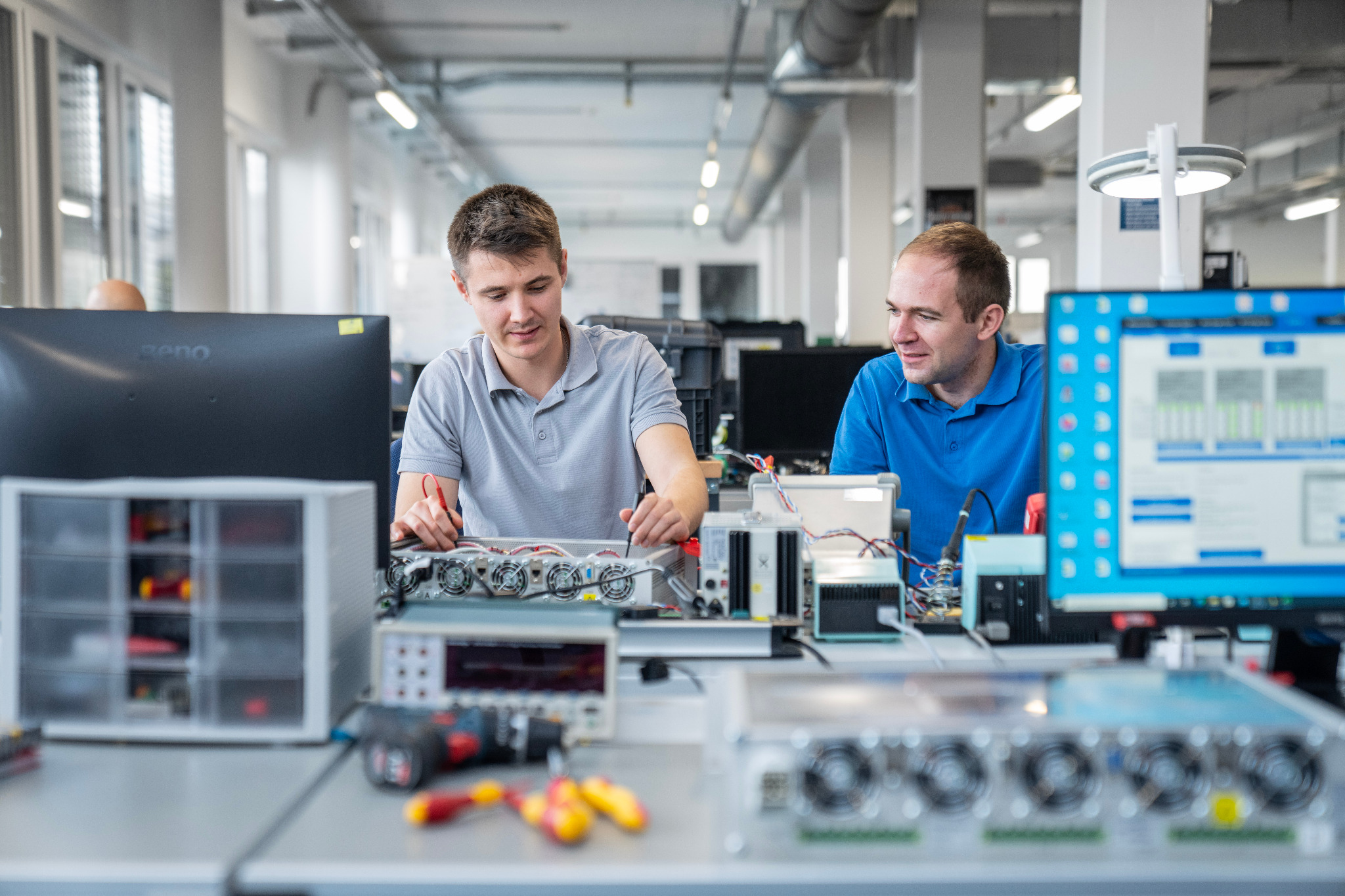 Zwei comemso-Mitarbeiter arbeiten an einem geöffneten elektronischen Prüfsystem.